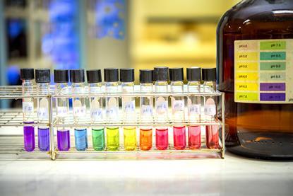 A photograph showing a range of solutions at different pH values; their colours correspond to the scale on a bottle of universal indicator solution
