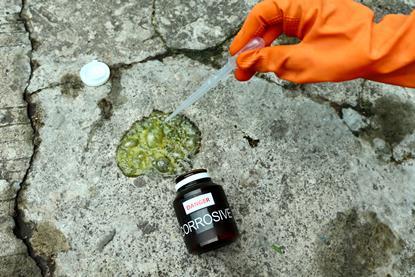 A photograph showing a bottle of acid spilled on a rock surface; a gloved hand holds a pipette over the spillage