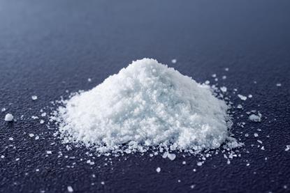 A close-up photograph of a heap of salt (sodium chloride) on a dark surface