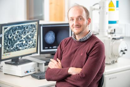 Szabolcs Pap is smiling in front of a computer in a lab.