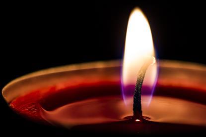 A macro photograph of a lighted candle, showing the flame and a pool of wax around the wick