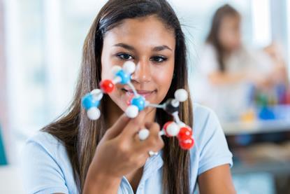 Female high school student studying molecule model in science class