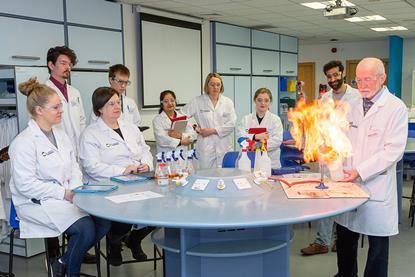 Students around a table watching an experiment conducted by teacher