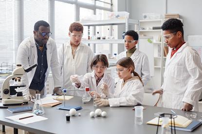 Students in a lab doing a practical and watched by their teacher