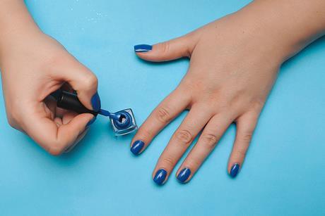 A close up of painting nails with blue polish