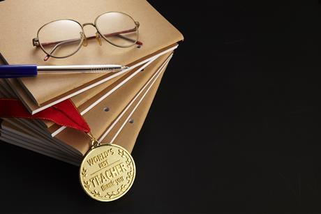 Photo of a pile of books, a pair of glasses, a pen and a medal with 'world's best teacher' written on it.