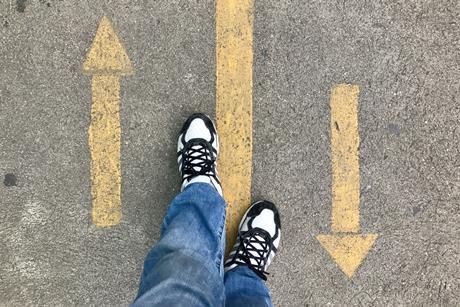 Looking down at feet between forward and backward arrows on a street