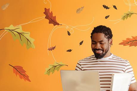 A man holding a laptop and some files smiles as he looks down at his computer. He is surrounded by illustrations of autumn leaves being blown in the wind. 