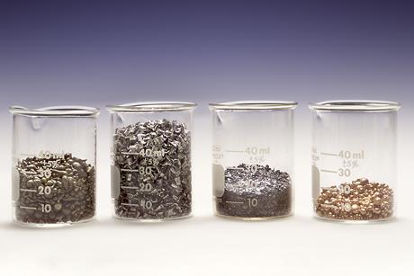 Four glass beakers holding different volumes of different metals 