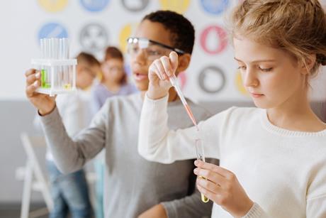 Two school pupils doing a chemistry experiment using pipettes and test tubes