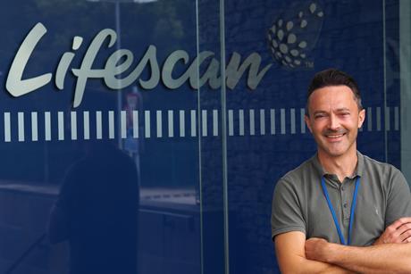 David Morris is smiling and wearing a grey top. A blue background with 'Lifescan' is behind him.