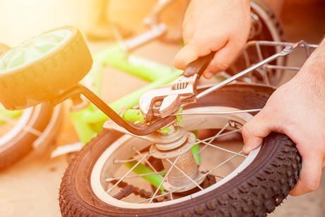 An adult using a spanner to remove training wheels from a child's bike