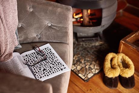An open crossword book in a comfy chair by a log burner and some warm slippers