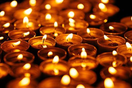 Numerous small candles or tealights burning against a dark background