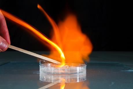 A hand igniting soap bubbles in a petri dish with a lit wooden split