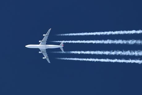 A passenger jet plane flying overhead leaving trails of vapour