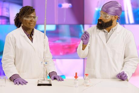 Two people in lab coats, safety goggles and latex gloves performing a titration