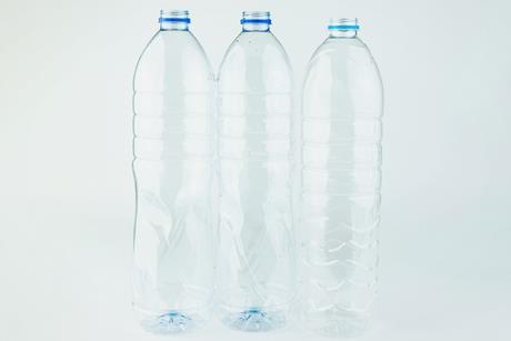 Three clear empty plastic drink bottles, against a plain white-grey background