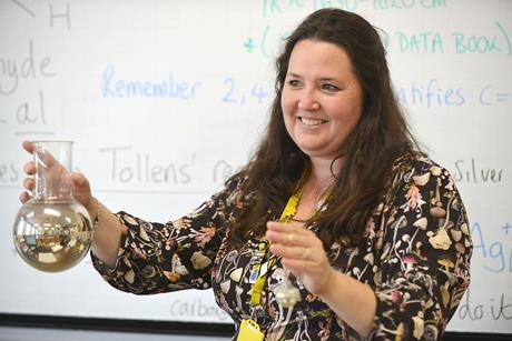 An image showing Jennifer Pierce wearing a black top with fungi on it and holding a round-bottom flask with a silver mirror