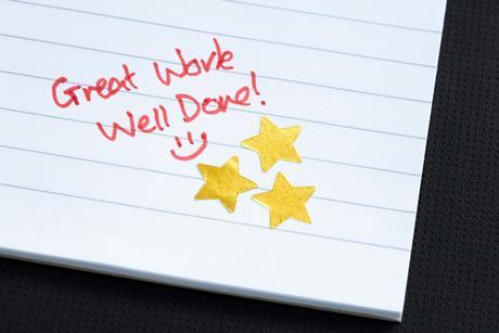 An exercise book with three gold stars and a "great work well done" written in red pen