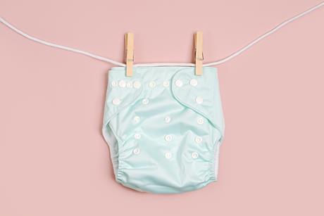 picture of a reusable cloth nappy on a washing line with a pink background