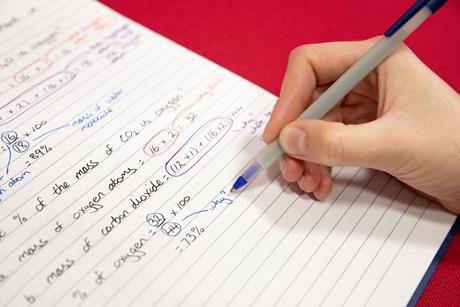 A hand writing chemistry equations with a ball point pen