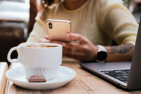 A woman with a tattoo on her arm typing on her mobile phone with a coffee and a chocolate