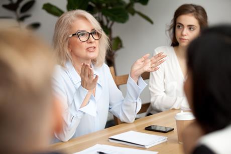 Photo of a woman explaining something  while sitting around a table with her colleagues