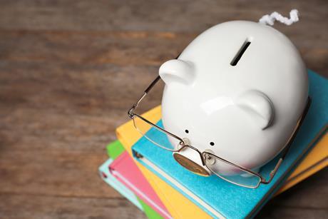 A white piggy bank with glasses sits on top of a file of different coloured books