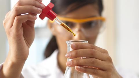 A student in a practical chemistry class, using a pipette to add an amber coloured liquid to a flask