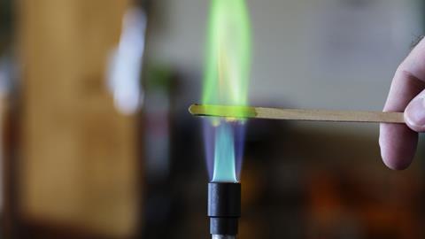 Copper solution burning on a wooden splint in a bunsen burner flame, producing a green flame