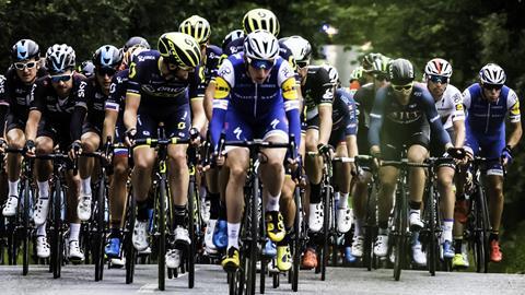A dozen male cyclists in a tight grouping pictured from the front
