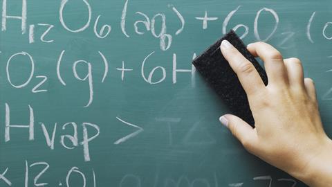 An image showing the hand of a teacher erasing chemical formulas from a blackboard