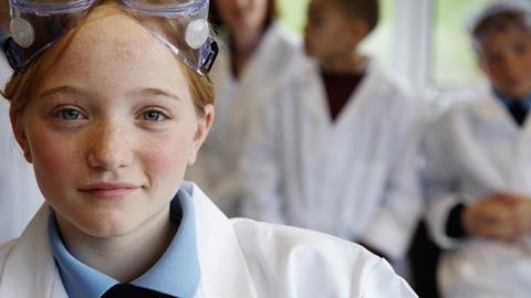 Young girl in lab coat with goggles and three other blurred people in the backgroung