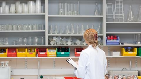 Female lab tech with clipboard looking at lab equipment