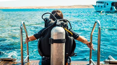 A scuba diver with an air tank sits on the edge of a boat ready to enter the ocean