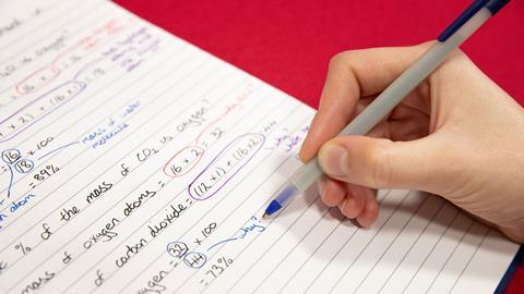 A hand writing chemistry equations with a ball point pen