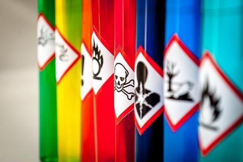 A row of test tubes containing brightly coloured liquids with warning signs on