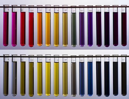 Two rows of test tubes containing liquids of different colours. The top shows a rainbow range from red through to dark purple and the bottom shows a muted range of dark greens and blues