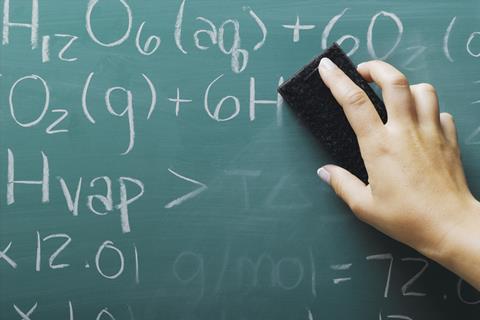 An image showing the hand of a teacher erasing chemical formulas from a blackboard