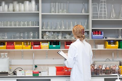 Female lab tech with clipboard looking at lab equipment