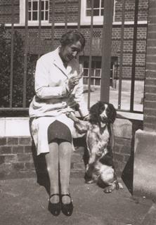 Scientist Marjory Stephenson wearing a lab coat sitting on a wall, next to a dog