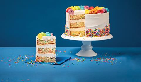 A colourful cake on a cake stand with a piece taken out to show the colourful candy inside