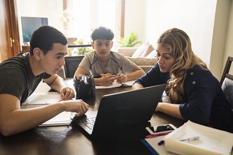 A photo of a mother helping her two teenage sons with schoolwork