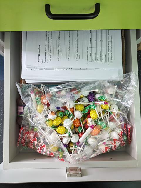 A draw of a desk containing exam papers and lollipops