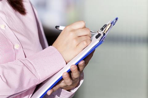 An image showing a woman taking notes on a clipboard