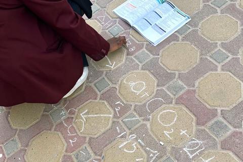 A student using chalk on the pavement to write chemical cycles