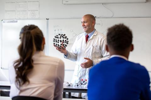 A chemistry teacher showing a high school class a model of buckminster fullerene