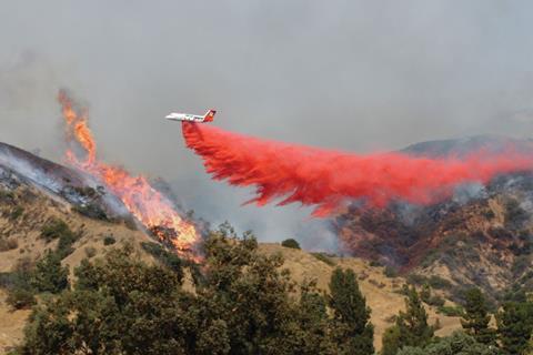 A small plane dropping a red fire retardant powder on the flames and smoke of a wildfire