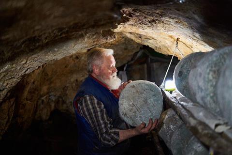 A man in a cave with a wheel of old cheese